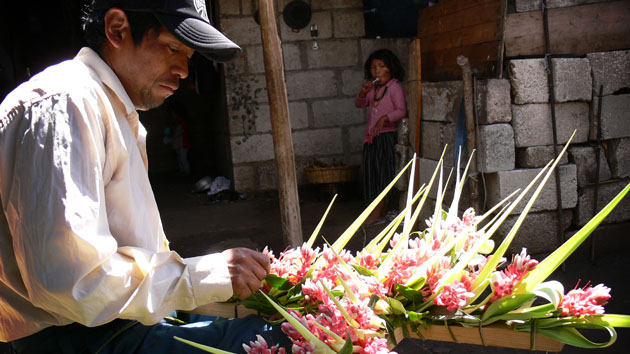 A man attaches pink flowers and broad folded leaves onto the frame of a cross