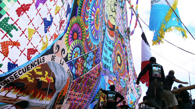 People stand near towering handmade kites, which include panels of words, patterns and pictures.